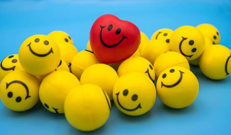 Red heart-shaped ball among yellow smiley faces on a blue background.